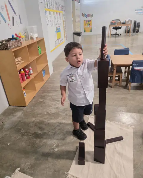 Niño de uniforme apilando bloques de la escalera marrón