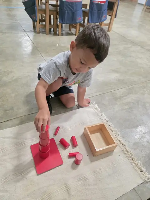 Niño armando la torre de cilindros rojos sobre la alfombra