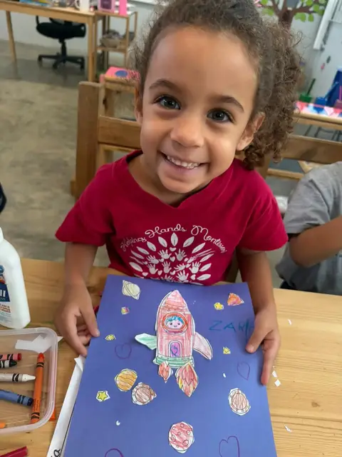 Niña sonriente con su lámina del cohete en el espacio