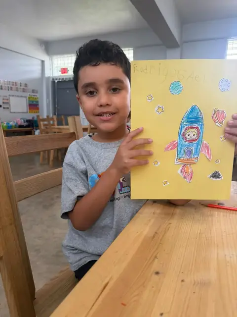 Niño presentando con orgullo su cohete espacial dibujado