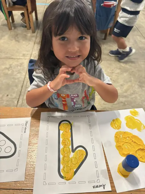 Niña haciendo un corazón con sus manos junto a su letra pintada