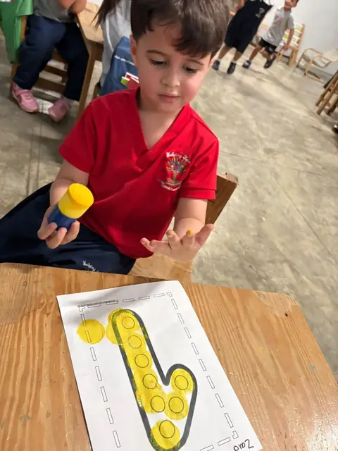 Niño de uniforme rojo estampando la letra con esponja amarilla