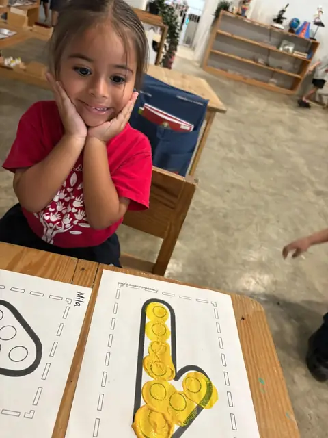 Niña sonriente junto a su letra terminada con pintura amarilla