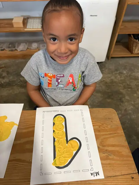 Niño con camiseta STEAM mostrando su letra pintada de amarillo