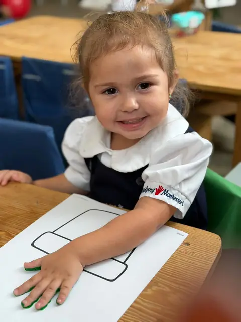 Niña sonriente con la mano pintada de verde sobre su lámina