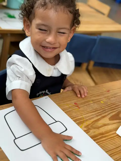 Niña riendo mientras estampa su mano en la hoja de trabajo