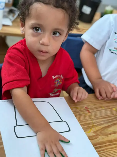 Niño con uniforme rojo trabajando su lámina con pintura verde