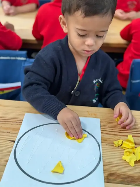 Niño pegando papel de seda amarillo dentro de su círculo