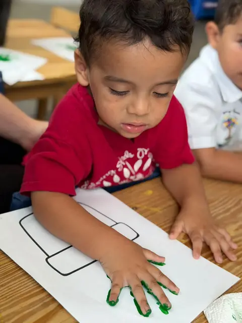Niño estampando su mano pintada de verde en la hoja de trabajo