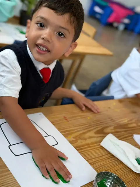 Niño sonriente mostrando su mano pintada de verde