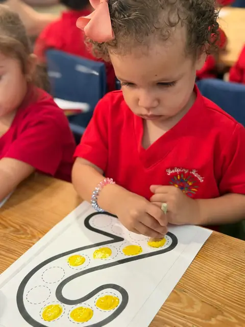 Niña llenando de amarillo los puntos del número dos