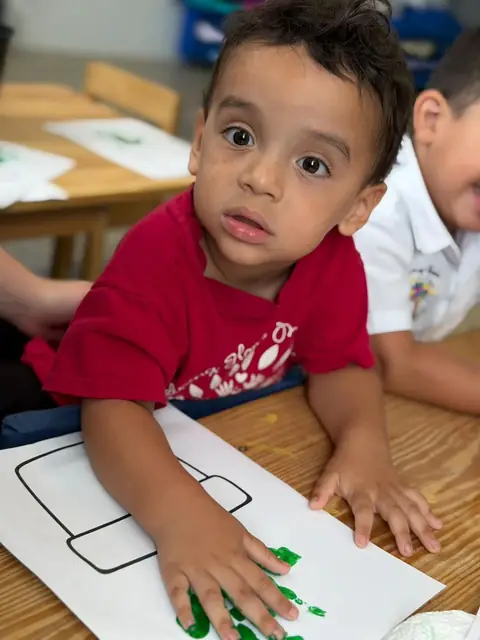Niño mirando a la cámara mientras estampa su mano en verde