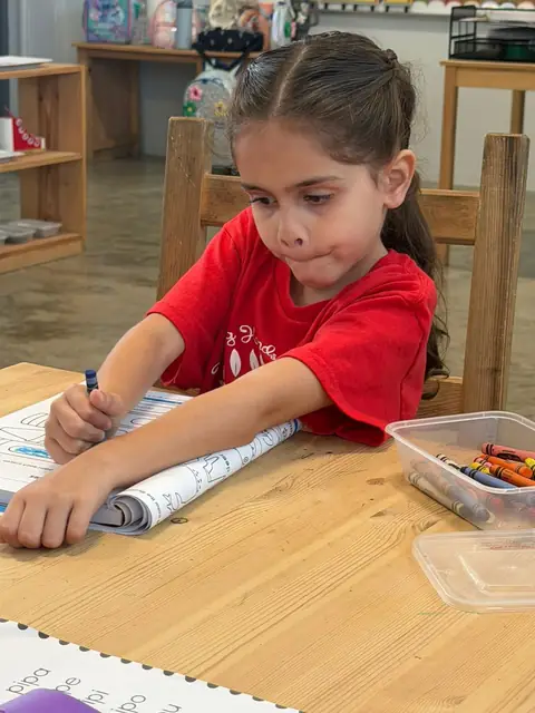 Niña coloreando con crayolas su hoja de trabajo