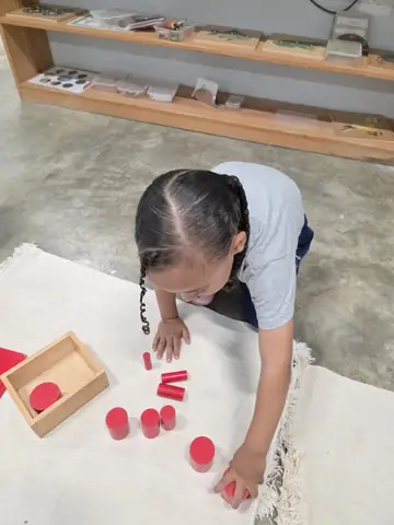 Niña ordenando los cilindros rojos sobre su alfombra de trabajo
