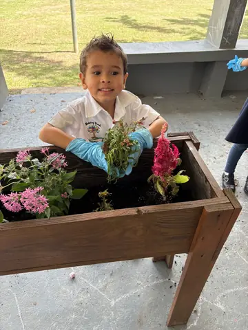 Niño sonriente plantando flores en el jardinera del patio