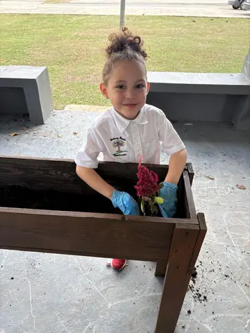 Niña sonriente plantando una flor roja en la jardinera