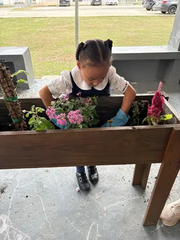 Niña regando las flores del jardín con sus guantes puestos