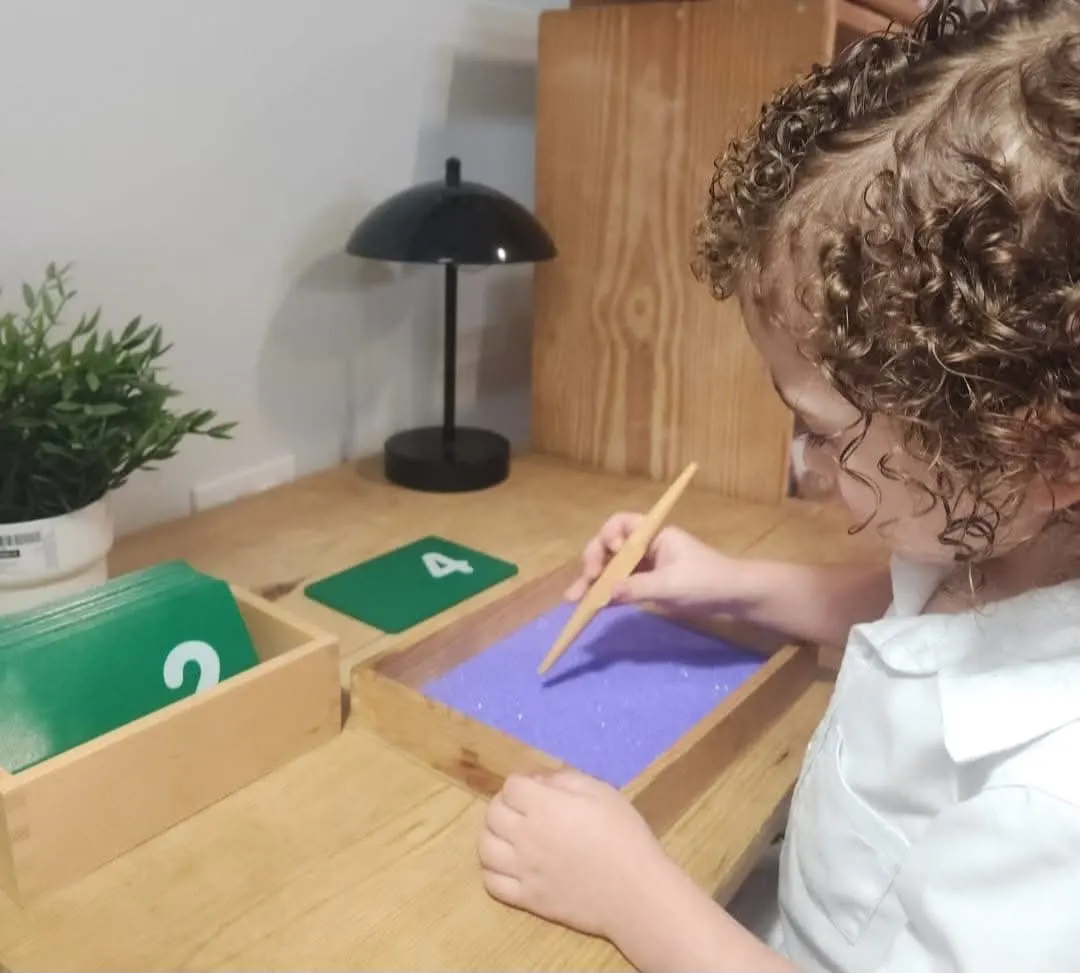 Estudiante practicando trazos y números en bandeja Montessori